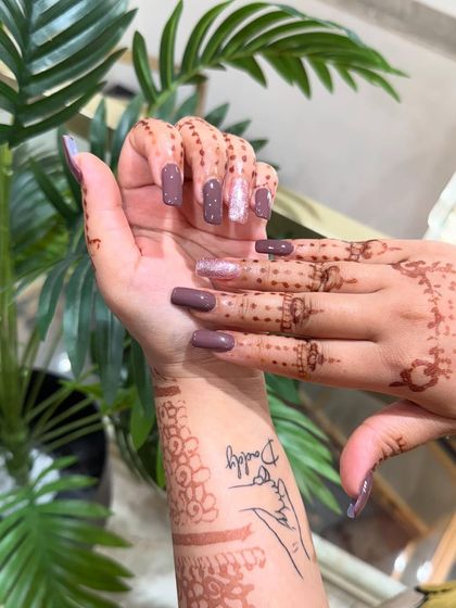 These long, square-shaped nail extensions provide a large canvas for both solid colors and art. Here they are shown in a solid mauve color with a single silver glitter accent nail, complementing the client's henna.