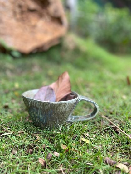 A stoneware mug with a rustic, textured finish, pictured here in the garden. I love creating pieces that feel connected to the earth they came from.