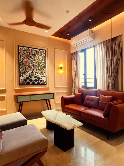 A closer look at the living area from image 51, focusing on the tan leather sofa and the Madhubani "tree of life" painting.