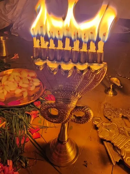 A close-up of a traditional multi-wick brass lamp, an essential part of the Durga Deepa Namaskara pooja. The light from these lamps symbolizes the dispelling of darkness and ignorance, bringing clarity and divine grace.