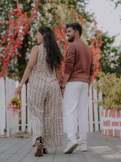 A casual stroll hand-in-hand along a path lined with a white picket fence and vibrant flowers. This image captures the simple, everyday romance that is the foundation of a great love story.