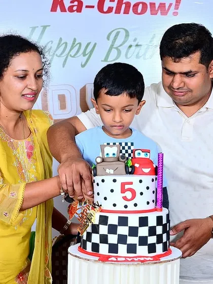 The family gathers to help the birthday boy cut his amazing race-themed cake.