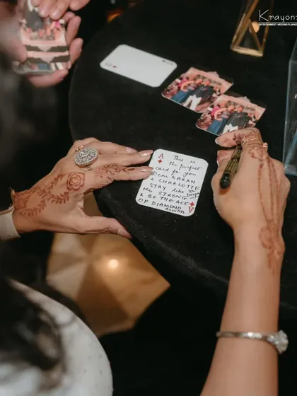A guest with beautiful mehendi writes a personal note on a custom playing card, a unique and memorable way to leave a message.