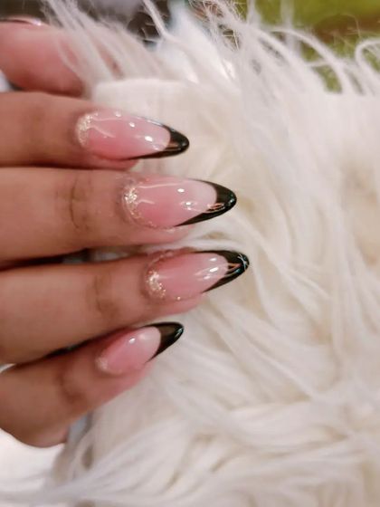 A sophisticated black French manicure on almond-shaped nails, with a subtle gold glitter line separating the tip from the natural base.