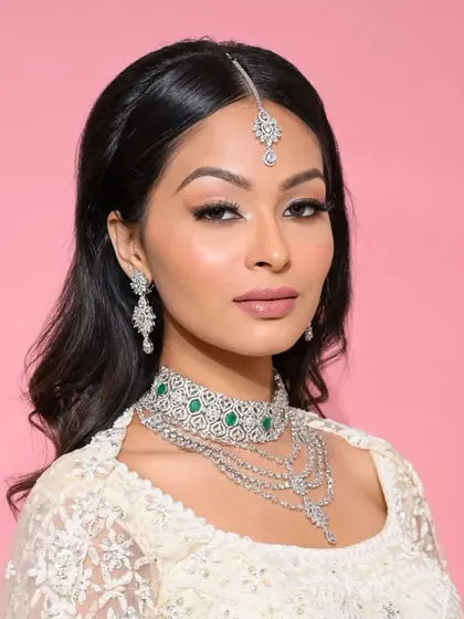 A model showcasing a complete diamond bridal look. This set features a layered diamond and emerald choker, a longer cascading necklace, matching earrings, and a maang tika for a truly glamorous and cohesive bridal style.