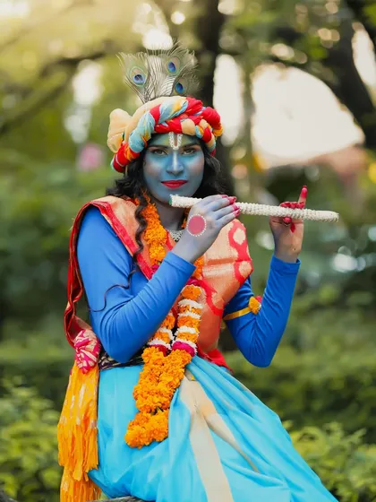 A solo portrait of the Krishna look, focusing on the vibrant blue body paint and traditional accessories.