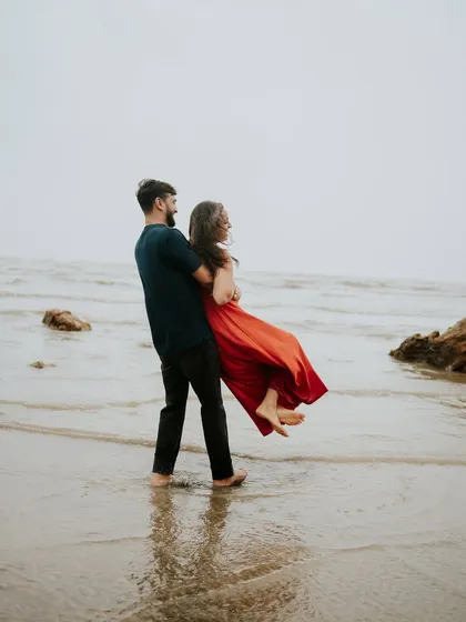 The groom lifts his bride-to-be in the shallow waters of the beach, a perfect shot for a fun and romantic couple photoshoot.