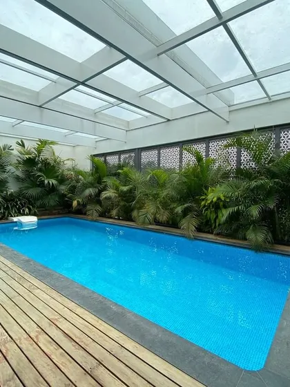 A semi-enclosed pool designed for a private residence, showcasing our versatility in creating serene wellness spaces. The design uses a translucent roof for natural light, lush greenery, and decorative screens to ensure privacy and tranquility.