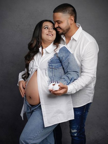 A joyful portrait of the couple holding up a tiny pair of baby shoes, a perfect prop for a casual shoot.