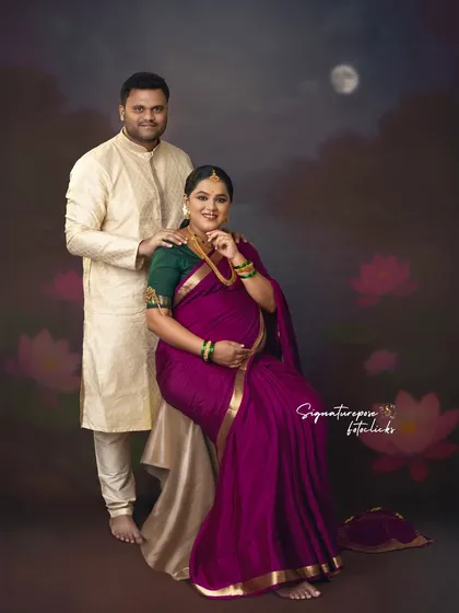 A classic couple's portrait where the partner stands beside the seated mother-to-be, both in traditional attire.