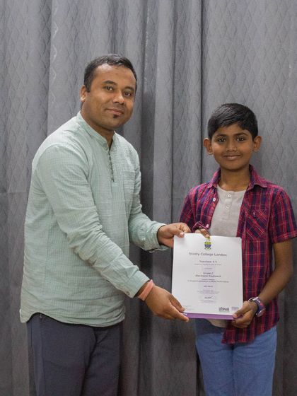 A student is awarded his Trinity College London certificate by his teacher.