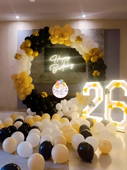 A classic black, gold, and white theme for a 26th birthday, featuring a balloon ring, neon sign, and marquee numbers.