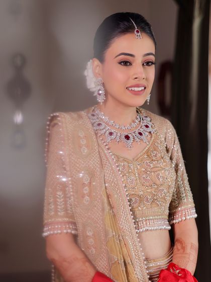 A reflective moment. The soft lighting highlights the flawless base and the intricate details of her bridal lehenga and jewelry.
