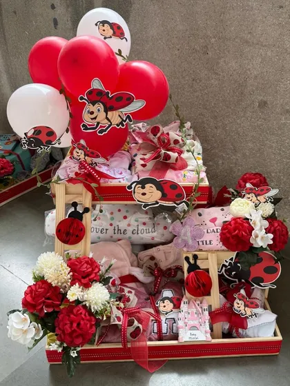 An adorable "ladybug-themed" baby hamper, perfect for a baby girl. This tiered arrangement is filled with clothing, essentials, and cute ladybug cutouts, all in a vibrant red and white color scheme.