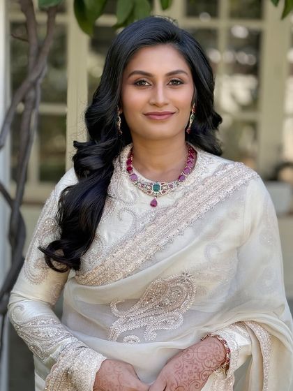 A simple, classic, and elegant look featuring a white saree, soft waves, and a pop of color from the ruby necklace.