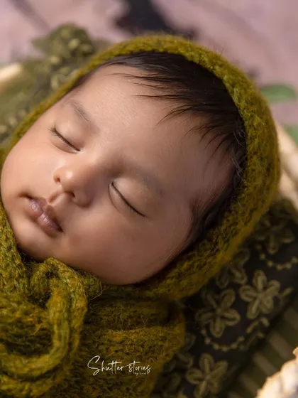 A detailed close-up of a baby in a green knit wrap and bonnet, highlighting the texture of the materials and the baby's delicate features.