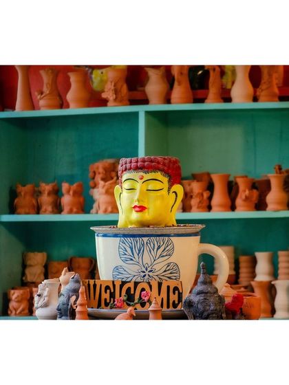 A serene Buddha head planter sits among other unpainted pottery pieces, waiting to be chosen and transformed. This is just one of the many unique items you can choose to paint.