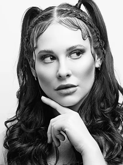 A black and white beauty portrait focusing on sculpted features and creative hair styling. The makeup enhances the model's bone structure, creating a strong and graphic look.