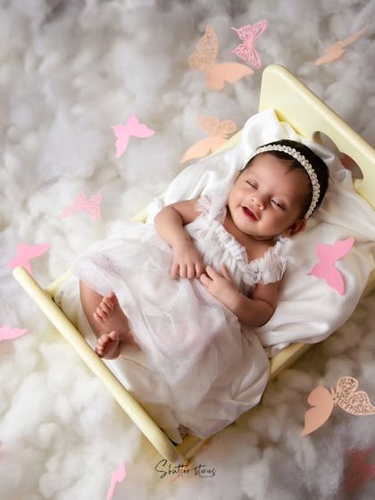 A dreamy, whimsical portrait of a smiling baby in a miniature bed, surrounded by clouds of cotton and paper butterflies. This demonstrates a more elaborate, creative setup.