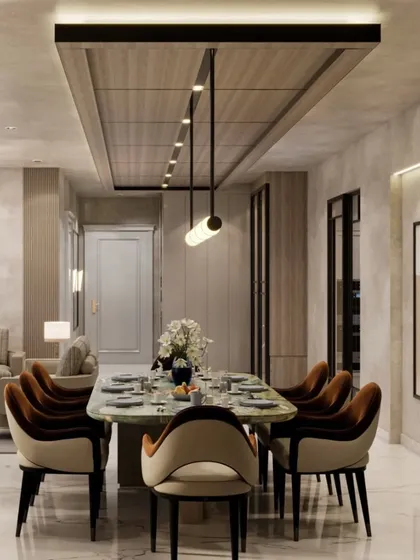 The dining area in this home features a stunning green marble table and plush velvet chairs. The space is defined by a wooden ceiling panel with integrated lighting, creating a sophisticated zone for shared meals.