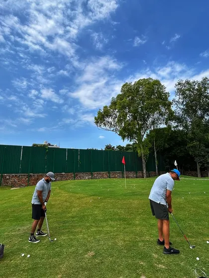 Two friends work on their chipping and pitching on our real turf short game area under a beautiful blue sky.