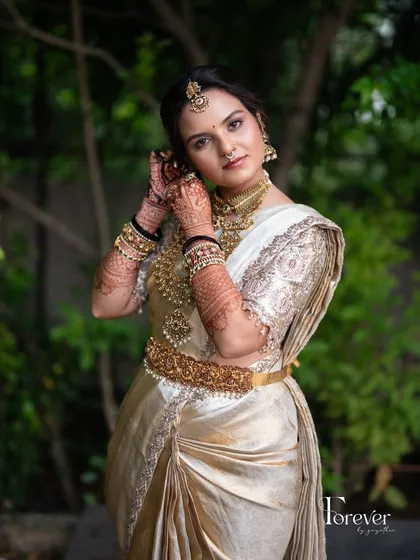 A candid moment of the client adjusting her earring, showcasing her henna-adorned hands and full attire.