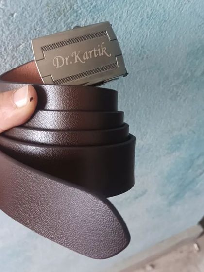 A personalized leather belt with the name 'Dr. Kartik' engraved on the buckle.