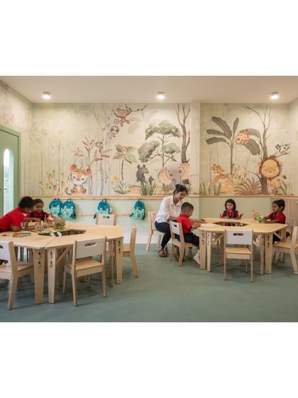 A teacher helps students in the forest classroom. The hexagonal table arrangement encourages collaboration and group work, demonstrating the flexibility of the modular furniture we chose.