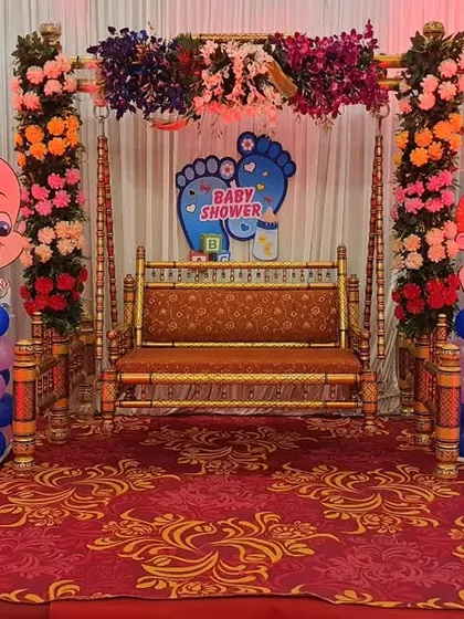 A baby shower setup at The GreenWood Banquet hall. This design uses a mix of real and artificial flowers on the jhula, with cute baby cutouts and pink and blue balloon pillars for the gender reveal theme.