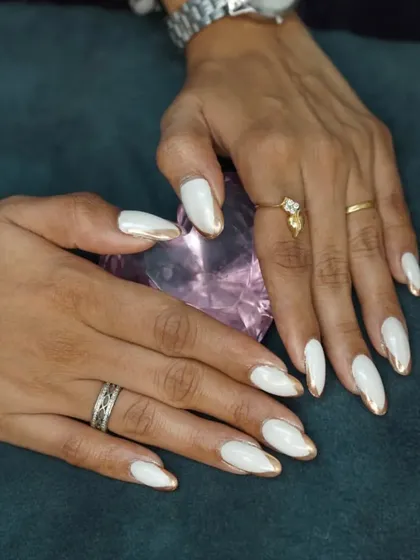 A clean and elegant look featuring almond-shaped nails with a crisp white base and a striking gold chrome edge. This is a popular choice for a sophisticated and polished style.