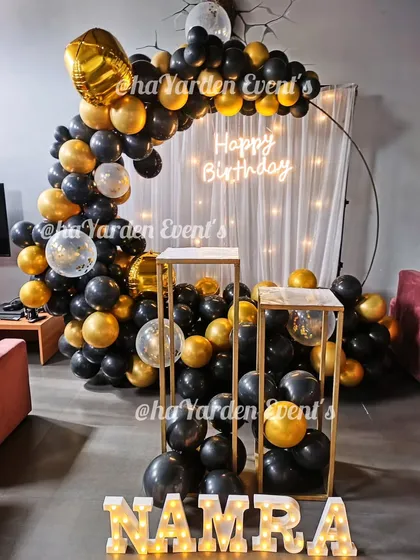 A chic black and gold half-ring balloon setup. The fairy light curtain and marquee letters add a touch of glamour to this home celebration.