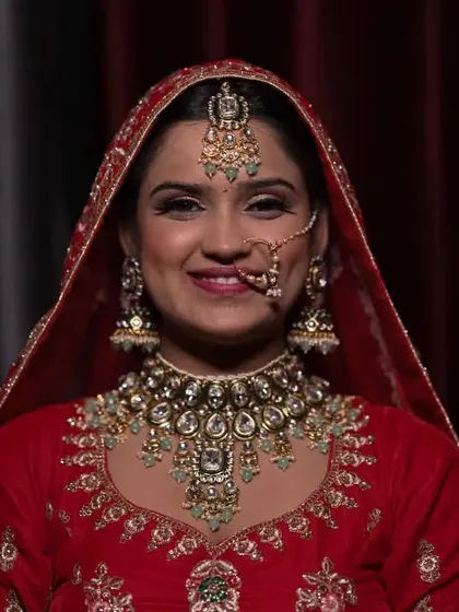 A classic, elegant portrait of a bride in her red wedding lehenga, looking directly at the camera with a gentle smile.