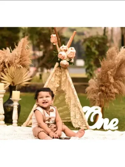 A full view of our outdoor boho-themed first birthday setup, complete with a lace teepee and pampas grass, set against the beautiful greenery of a park.