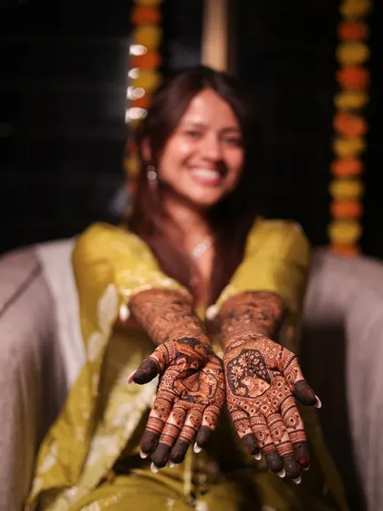 A joyful bride showing her palms, each telling a different part of her story through custom portrait mehendi.