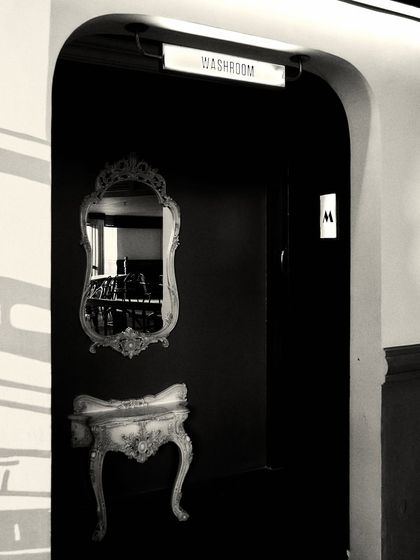 A grayscale shot of our Jollygunj bar project in Bangalore. We used dramatic lighting and an antique-style mirror to create a moody, atmospheric entrance to the washroom.