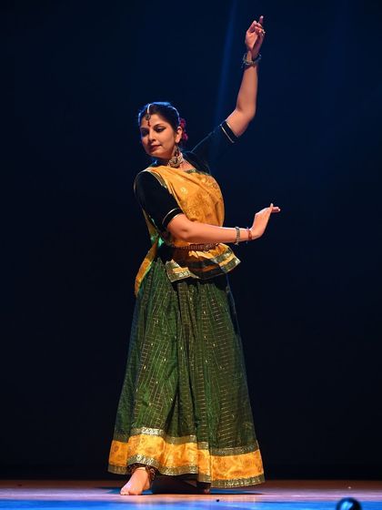 Performing on stage in a traditional green and yellow costume. This pose captures the grace and control that are fundamental to the Jaipur Gharana style of Kathak.