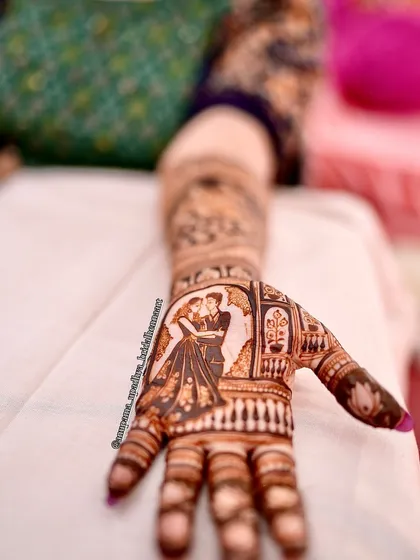 A close-up of a romantic couple figure on the bride's palm. This is the heart of her mehandi story, a celebration of her love.