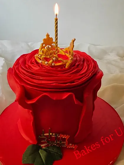 A stunning sculpted cake designed to look like a blooming red rose. The delicate petals are crafted from fondant, and a single lit candle emerges from the center.