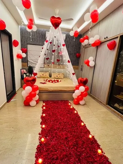 This is my signature romantic room setup. It features a stunning floor path made of real rose petals leading to the bed, which is decorated with a heart shape and a beautiful canopy lit with warm fairy lights. The red and white balloons on the ceiling and floor complete the look, creating an unforgettable surprise for your partner.