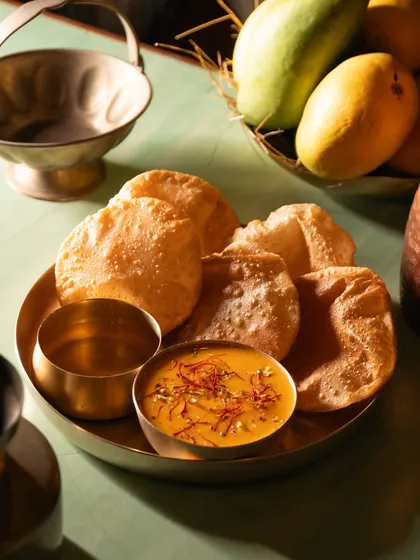 Aamras puri, a seasonal mango delicacy. The vibrant yellow of the mango puree contrasts beautifully with the brass plate.