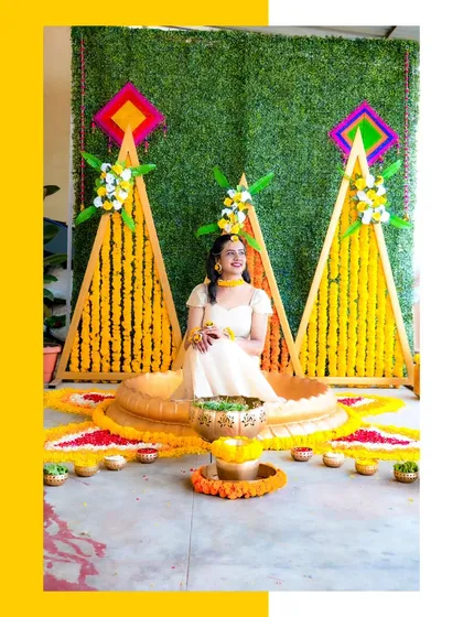 A full view of the bride seated in her beautiful Haldi ceremony setup. The geometric backdrop with marigold garlands creates a modern yet traditional look.