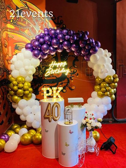 A stylish 40th birthday setup with a purple, white, and gold balloon ring. The 'Happy Birthday' neon sign and marquee letters for the initials add a personal touch.