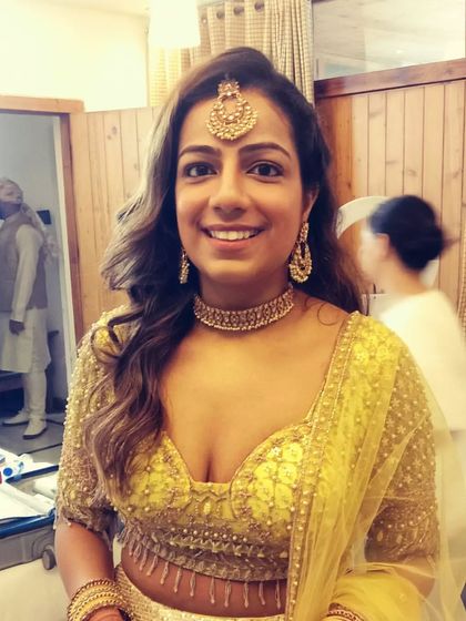 A happy bride with her hair in a simple, open style with soft waves and a maang tikka. This is a great look for a Haldi or Mehendi ceremony.