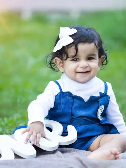 The biggest smile for her first birthday. Holding the 'One' sign, this happy baby is the star of her milestone photoshoot, captured in beautiful natural light.