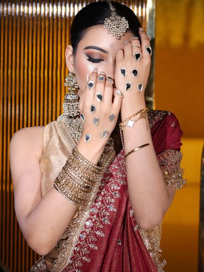 A close-up of the bride's hands and face, showing the unique mirror-work hand accessory and the sharp, winged eyeliner.