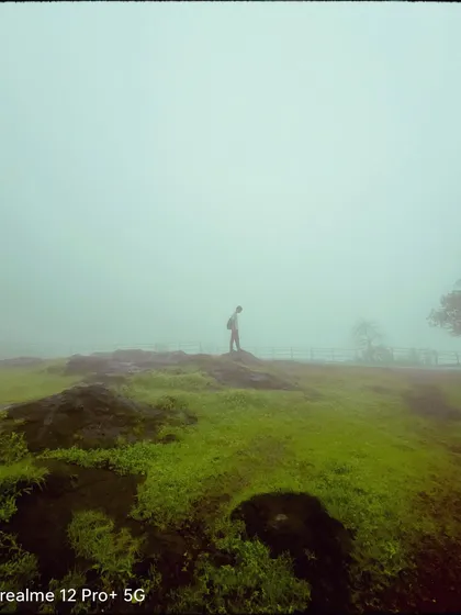 A lone figure stands on a rocky, green hill enveloped in thick fog. This minimalist composition from Matheran evokes a sense of solitude, adventure, and being on top of the world, even if the view is obscured.