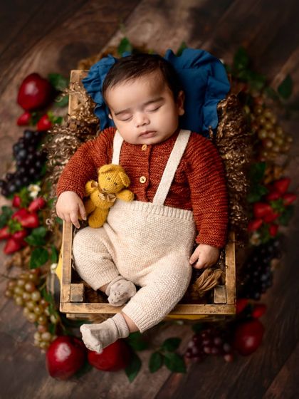 A cozy autumn-themed setup with a baby in a knitted outfit, nestled in a crate surrounded by fruit. The warm tones create a rich and inviting portrait.