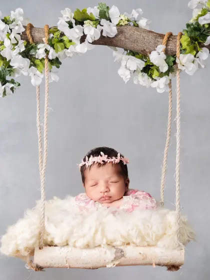 An angelic newborn portrait featuring a baby sleeping on a fluffy cloud-like swing, decorated with a branch of white flowers. This setup creates a serene and dreamy atmosphere.