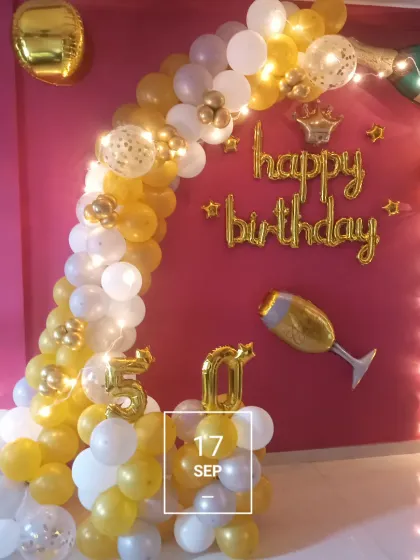 A gold and white balloon arch with fairy lights, perfect for celebrating a 50th birthday at home.