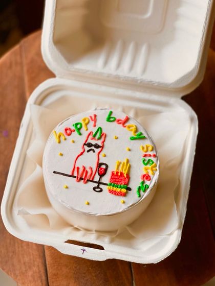 A fun and colorful birthday cake for a sister, featuring a cool cat with sunglasses, a glass of wine, and fries. The multi-colored "happy bday sis" text adds to the playful vibe.